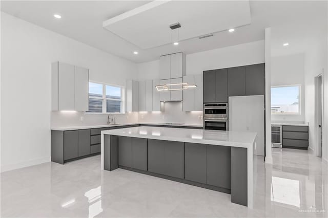 kitchen featuring light countertops, modern cabinets, black electric stovetop, beverage cooler, and a center island