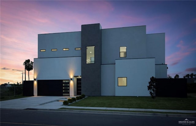contemporary home featuring driveway, stucco siding, a yard, and an attached garage