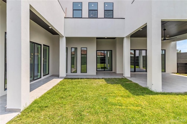 rear view of house with a lawn, ceiling fan, stucco siding, and a patio area
