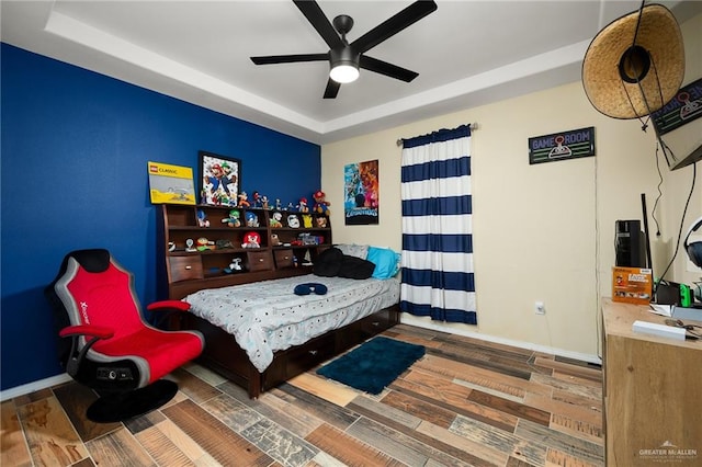 bedroom with hardwood / wood-style flooring, ceiling fan, and a tray ceiling