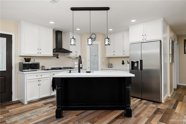 kitchen featuring stainless steel appliances, wall chimney range hood, wood-type flooring, white cabinetry, and an island with sink