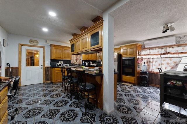 15668 Primera Rd, Harlingen, TX 78552 - kitchen featuring a wall mounted air conditioner, a textured ceiling, dark countertops, brown cabinets, and glass insert cabinets