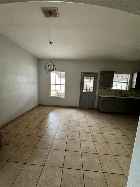 unfurnished dining area with an inviting chandelier, a wealth of natural light, sink, and light tile patterned floors