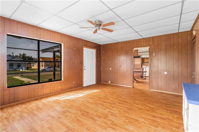 empty room with a ceiling fan, light wood-type flooring, a drop ceiling, and baseboards