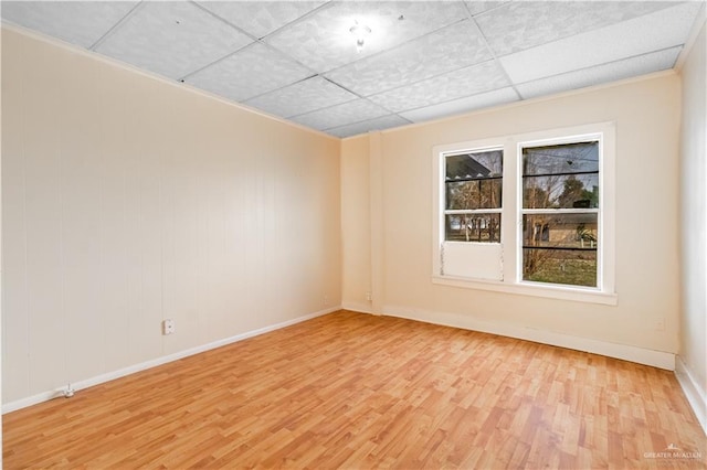 empty room featuring a paneled ceiling, baseboards, and light wood-style flooring