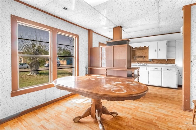 unfurnished dining area with a paneled ceiling, baseboards, light wood finished floors, and wallpapered walls