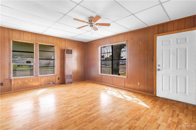 interior space with a drop ceiling, wood walls, ceiling fan, and wood finished floors