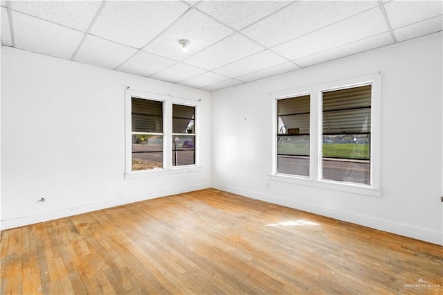 empty room with hardwood / wood-style flooring, a paneled ceiling, and baseboards