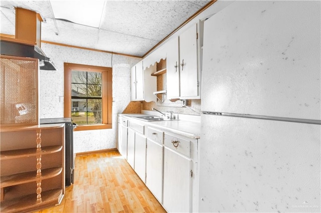 kitchen featuring light wood finished floors, light countertops, freestanding refrigerator, white cabinets, and a sink