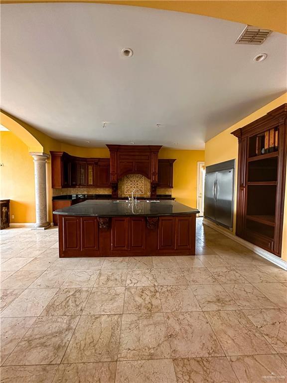 4132 Cosentino Dr, Mcallen, TX 78504 - kitchen featuring built in refrigerator, arched walkways, ornate columns, tasteful backsplash, and a kitchen island with sink