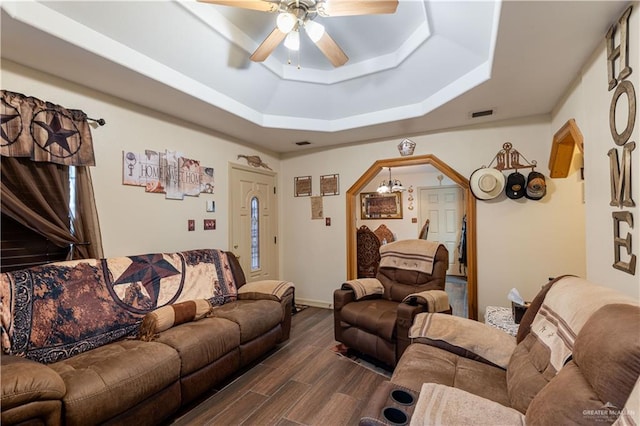 living room with a tray ceiling, dark hardwood / wood-style floors, and ceiling fan with notable chandelier