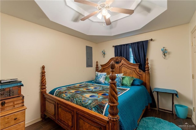 bedroom with dark wood-type flooring, ceiling fan, a tray ceiling, and electric panel