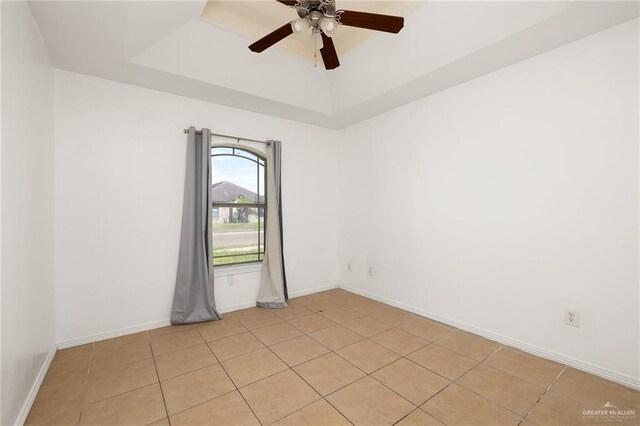 empty room featuring a raised ceiling, ceiling fan, and light tile patterned flooring