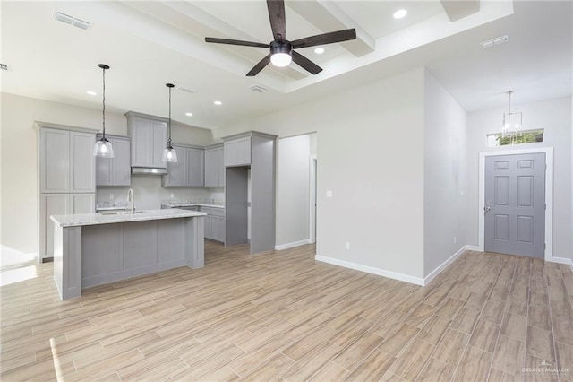 kitchen with gray cabinetry, light stone countertops, an island with sink, and light hardwood / wood-style flooring