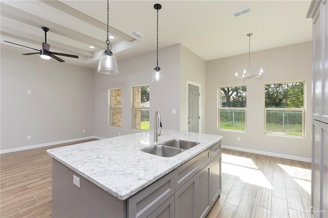 kitchen with a kitchen island with sink, sink, light stone countertops, and light hardwood / wood-style flooring