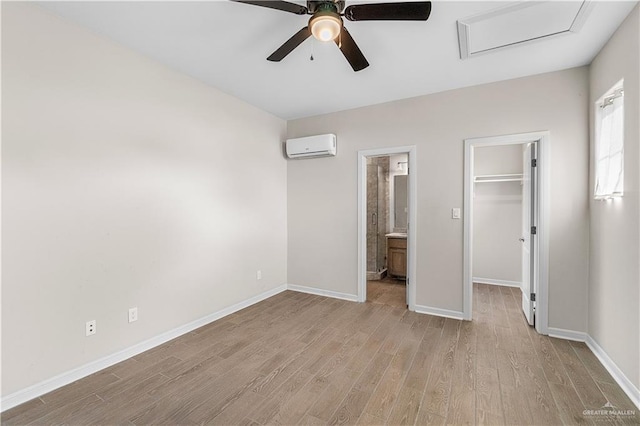 unfurnished bedroom with a wall mounted air conditioner, a walk in closet, ceiling fan, light hardwood / wood-style floors, and a closet