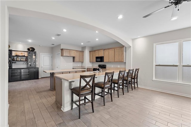 kitchen with light stone countertops, light brown cabinets, light hardwood / wood-style floors, a kitchen bar, and black appliances