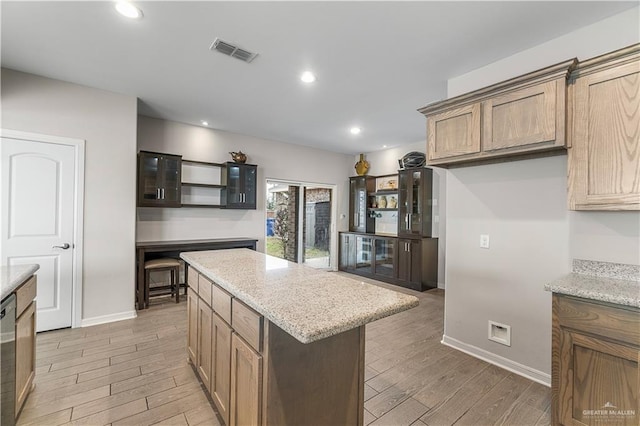 kitchen featuring light stone counters, dishwasher, a kitchen island, and hardwood / wood-style flooring