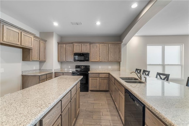 kitchen featuring black appliances, sink, light hardwood / wood-style flooring, light stone counters, and a breakfast bar area