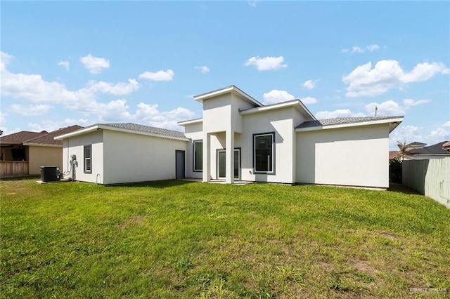 rear view of house with stucco siding, central AC, a lawn, and fence