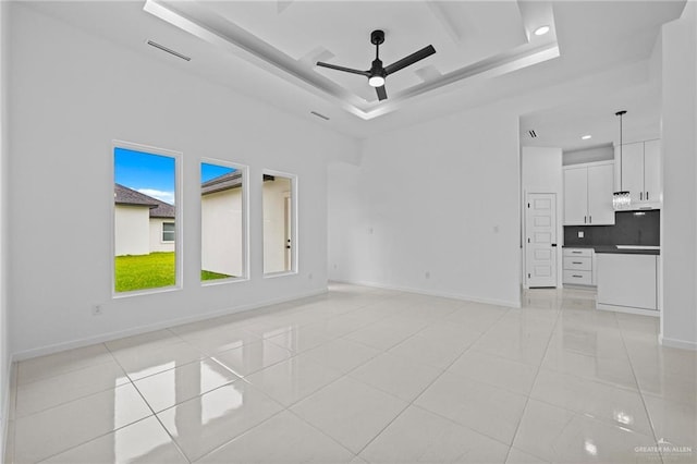 unfurnished living room with light tile patterned floors, baseboards, a raised ceiling, and ceiling fan