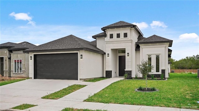 prairie-style house with an attached garage, stucco siding, a shingled roof, a front lawn, and concrete driveway