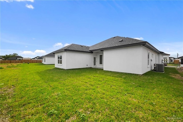 rear view of house with stucco siding, central air condition unit, a lawn, and a shingled roof