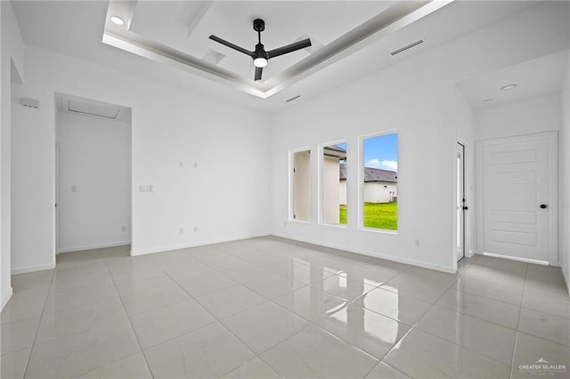 unfurnished room featuring visible vents, a raised ceiling, a ceiling fan, light tile patterned floors, and baseboards