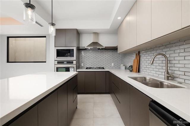 kitchen with stainless steel appliances, light countertops, a sink, and wall chimney exhaust hood