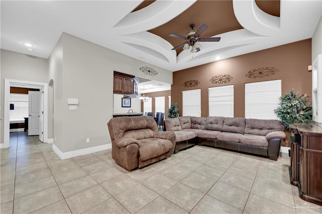 tiled living room with ceiling fan and a raised ceiling