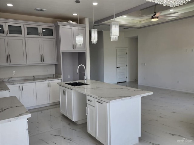 kitchen with white cabinetry, ceiling fan, sink, hanging light fixtures, and an island with sink