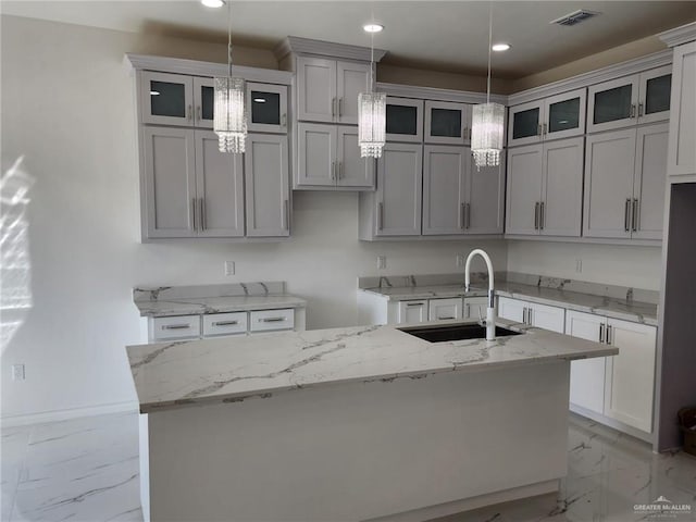 kitchen featuring gray cabinetry, light stone countertops, sink, pendant lighting, and a kitchen island with sink