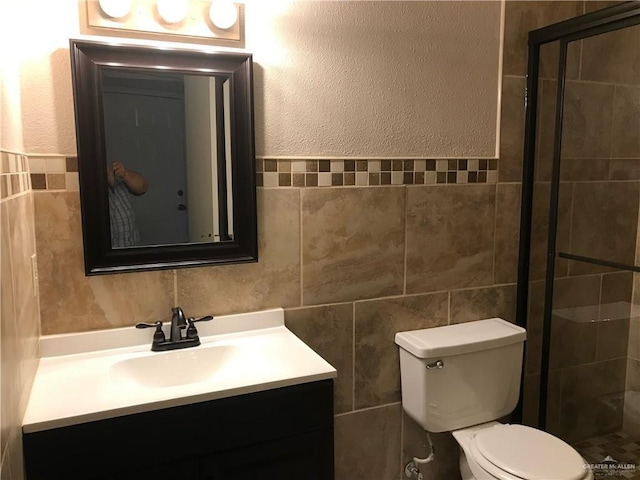 bathroom featuring tile walls, vanity, a shower with door, and toilet