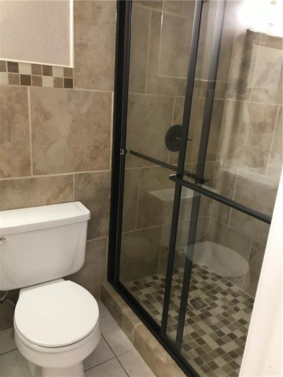 bathroom with tile walls, a shower with door, tile patterned floors, and toilet