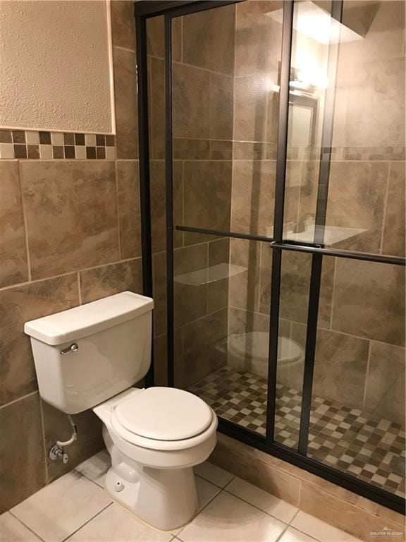 bathroom with walk in shower, toilet, tile patterned flooring, and tile walls