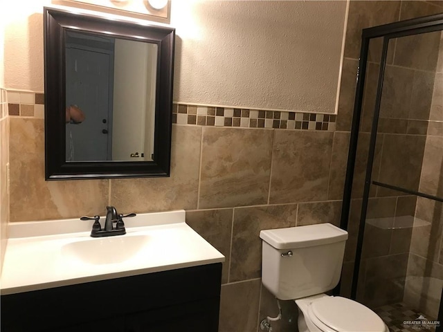 bathroom with vanity, tiled shower, tile walls, and toilet