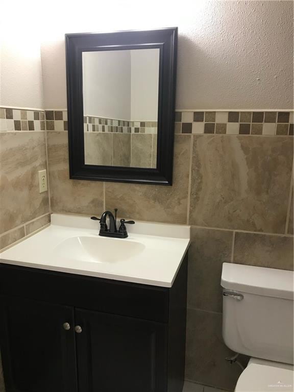 bathroom featuring vanity, tile walls, and toilet