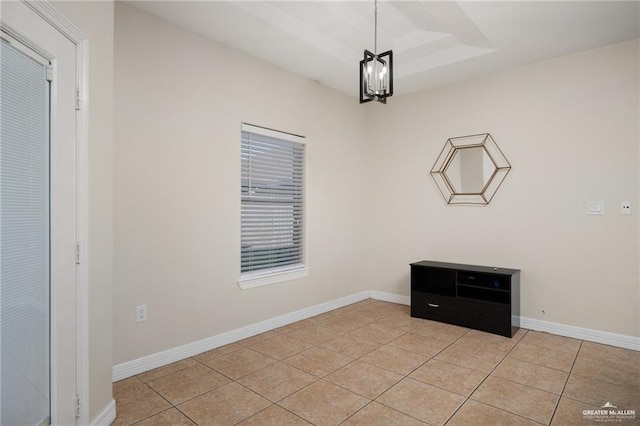 spare room with a tray ceiling, a chandelier, and light tile patterned flooring