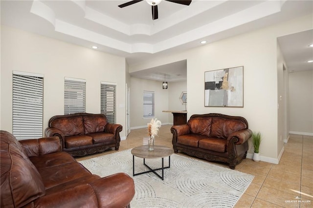 living room featuring a raised ceiling, light tile patterned flooring, and ceiling fan