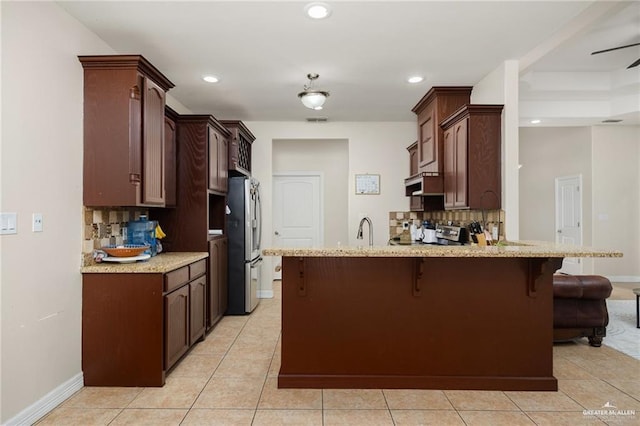 kitchen with sink, a breakfast bar area, stainless steel refrigerator, decorative backsplash, and kitchen peninsula