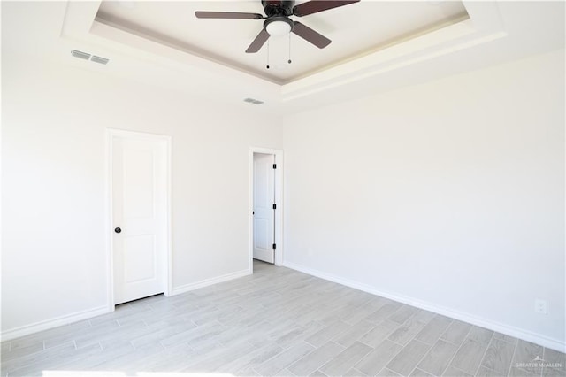 unfurnished room featuring ceiling fan, a raised ceiling, and light hardwood / wood-style floors