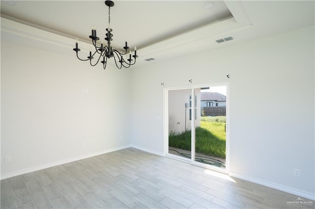 unfurnished room featuring a chandelier, a raised ceiling, and light wood-type flooring