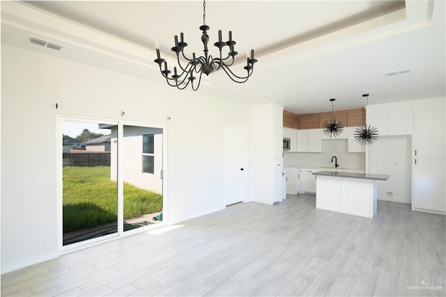 kitchen with pendant lighting, a raised ceiling, a kitchen island, and white cabinets