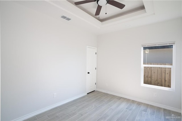 empty room with ceiling fan, a raised ceiling, and light hardwood / wood-style flooring