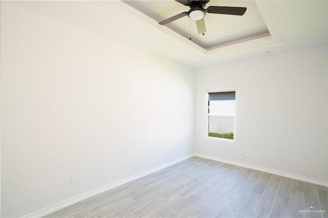 spare room with a raised ceiling, ceiling fan, and light wood-type flooring