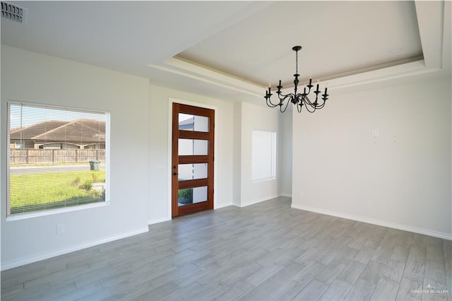 spare room featuring a tray ceiling, a chandelier, and light wood-type flooring