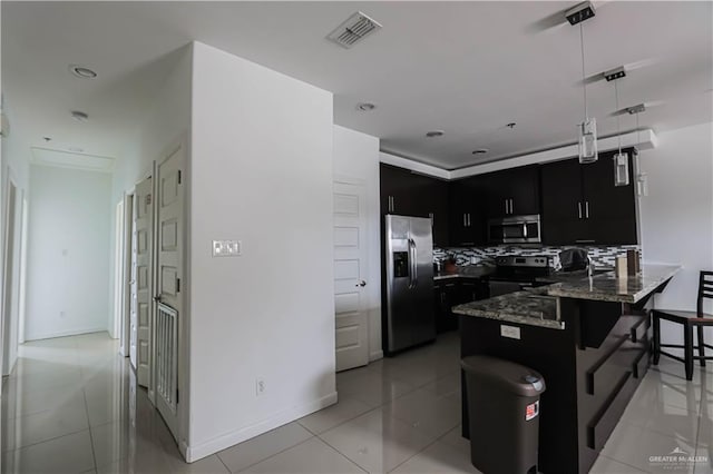 kitchen featuring dark cabinets, stainless steel appliances, a peninsula, visible vents, and a kitchen bar