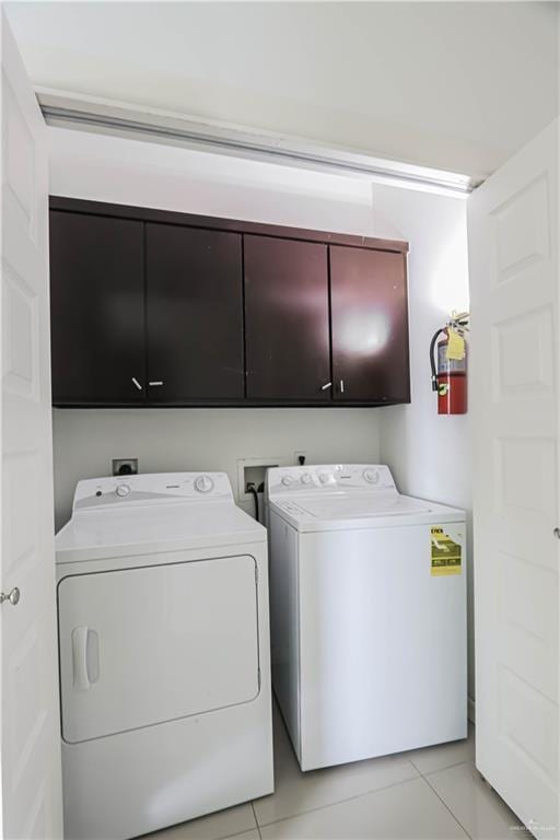 clothes washing area with cabinet space, washing machine and clothes dryer, and light tile patterned floors