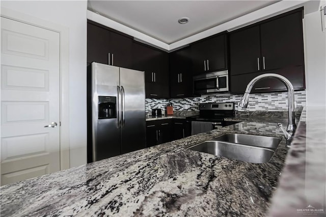 kitchen featuring tasteful backsplash, appliances with stainless steel finishes, a sink, dark stone countertops, and dark cabinets