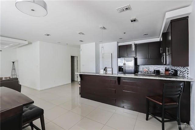 kitchen featuring tasteful backsplash, visible vents, stainless steel fridge with ice dispenser, light stone counters, and a kitchen bar